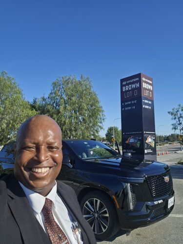 Patrick W. Paige, Founder of Ride N' Relax, standing next to his fleet Cadillac Escalade at SoFi Stadium.